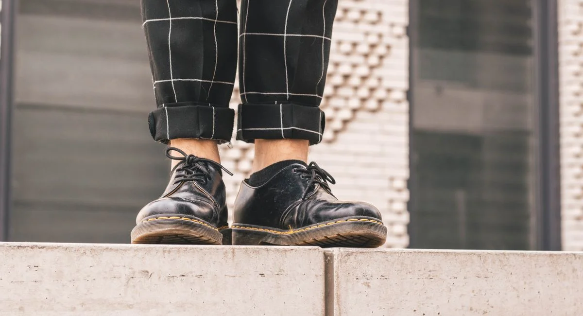 Close-up of black leather shoes on a concrete ledge against a modern city backdrop.
