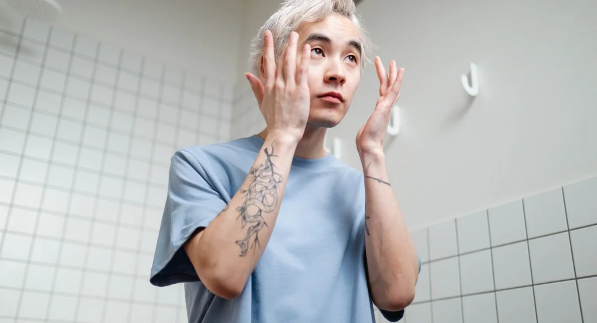 Young man applying skincare product in a contemporary bathroom setting.