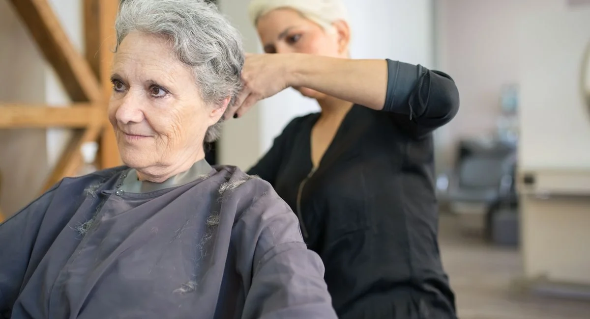 A senior woman receives a haircut at a salon, showcasing a skilled hairstylist in action.
