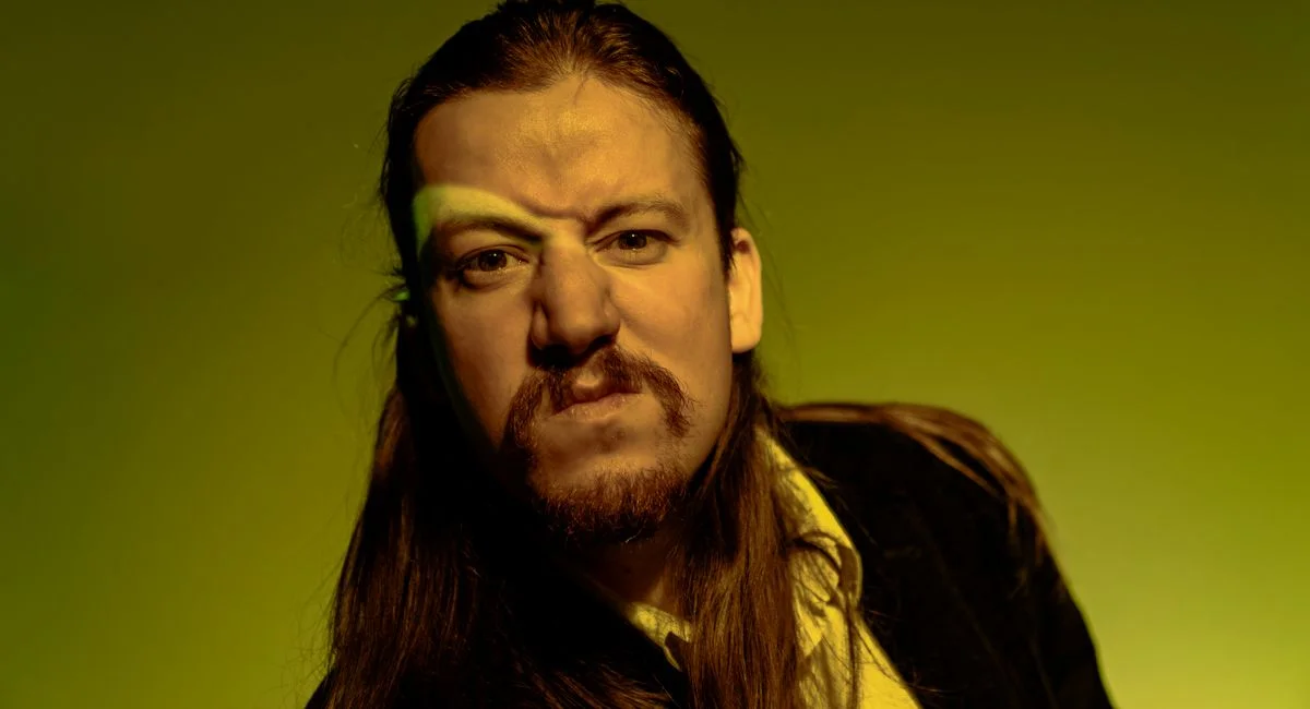 Dramatic portrait of a man with long hair and beard under intense yellow lighting.