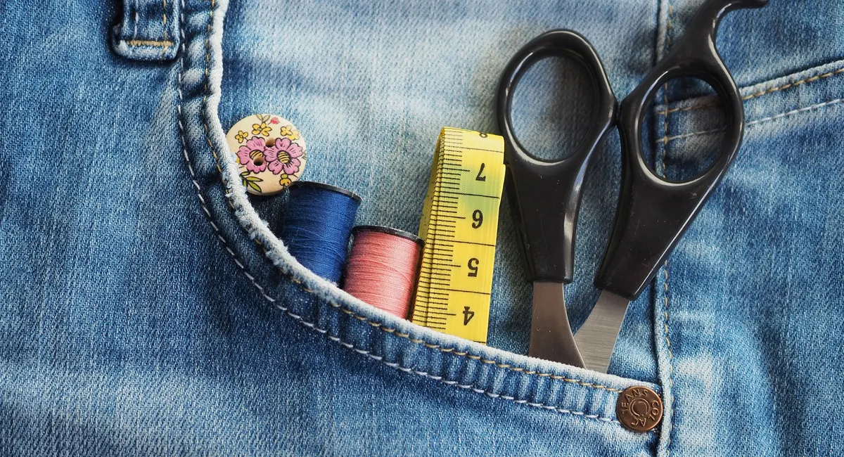 Outils utilisés pour couper un jean en short homme : ciseaux, mètre, craie sur un plan de travail