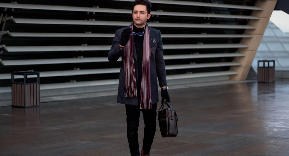 A fashionable man with a briefcase and scarf walking near modern architecture in Tehran.
