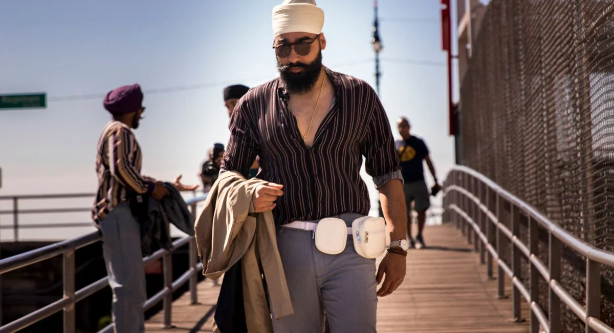 Stylish man with turban and sunglasses walking on Coney Island boardwalk in summer.