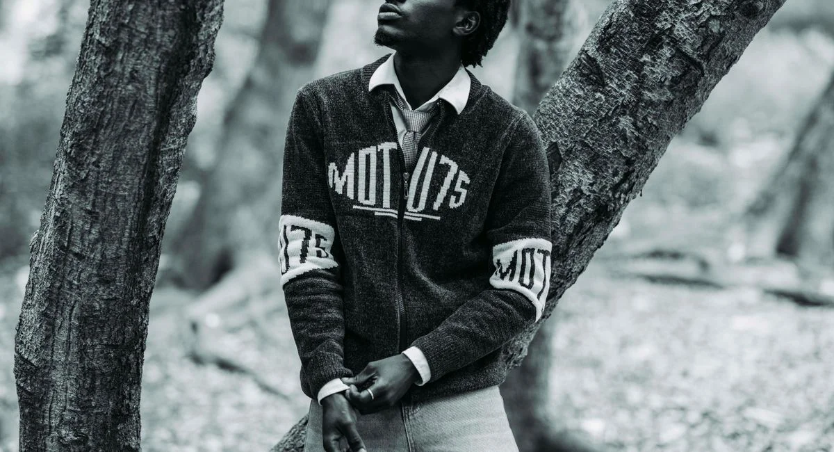 Black and white portrait of a young man in a forest, showing thoughtful expression and casual style.
