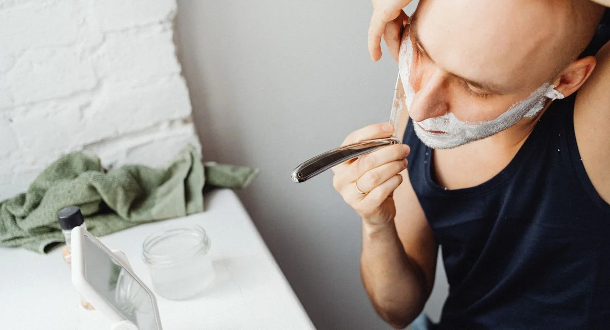 Bald man using straight razor and shaving cream in an indoor setting.