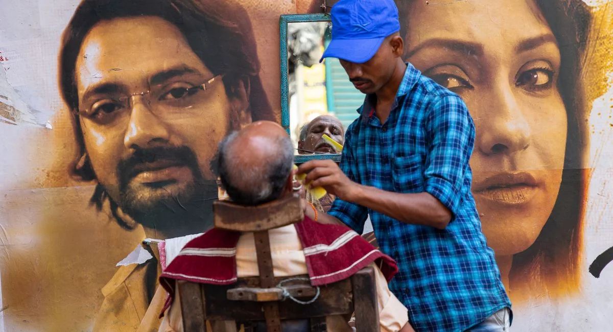 A street barber shaving a client's face in an outdoor setting with reflective mirror and artistic backdrop.