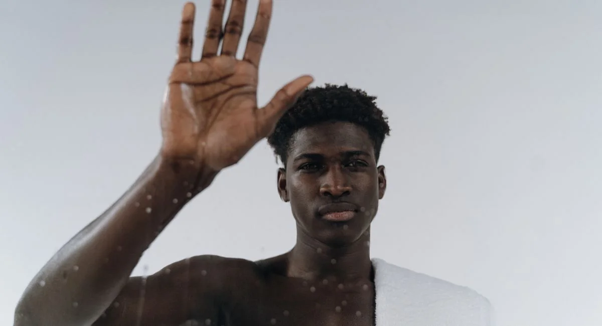 Adult black man with towel touching glass, creating a modern and reflective mood indoors.