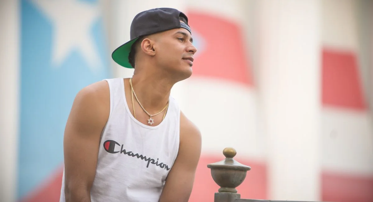 Stylish young man in a sleeveless shirt leaning on a railing outdoors.