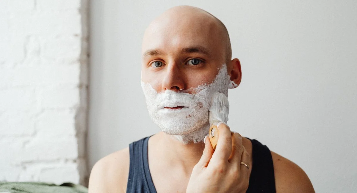 Bald man applying shaving cream with brush. Close-up indoor portrait.