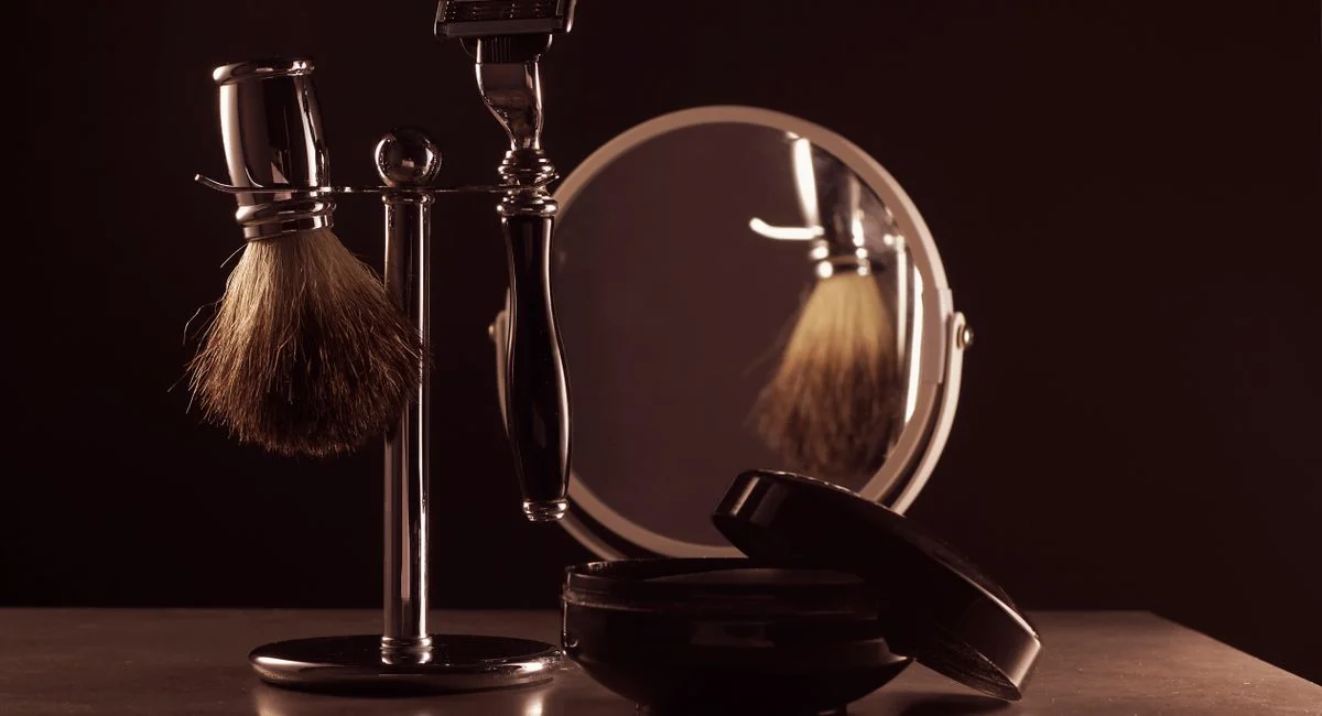 Stylish shaving set featuring a brush, razor, and mirror on a table, ideal for men's grooming.