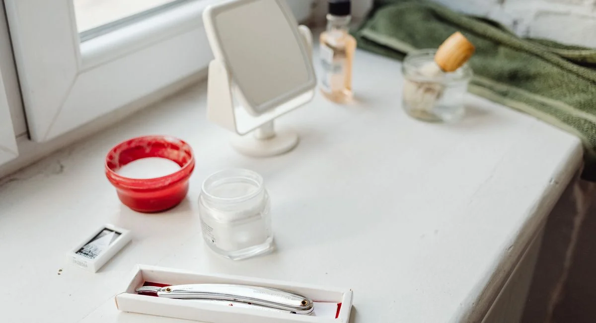 A traditional shaving kit with a razor, brush, and mirror on a bathroom counter.