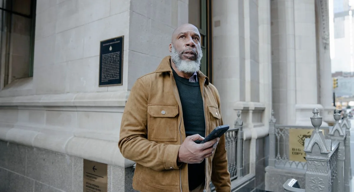 Stylish mature man with a gray beard using a smartphone on a city street.