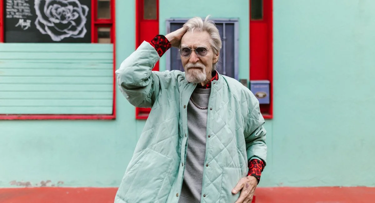 Fashionable senior man in a mint quilted coat posing in a vibrant urban background.