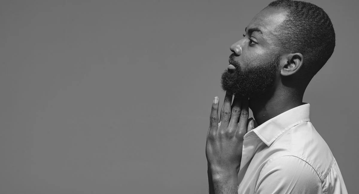 Black and white studio portrait of a stylish bearded man in a contemplative pose.