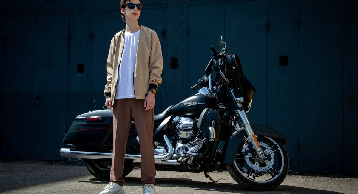 Man in casual fashion poses with motorcycle outdoors, showing urban style.