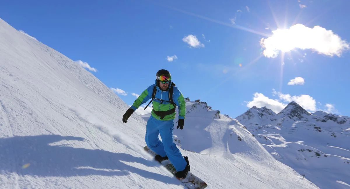 Dynamic shot of a snowboarder carving through snow on a bright winter day in the Alps.