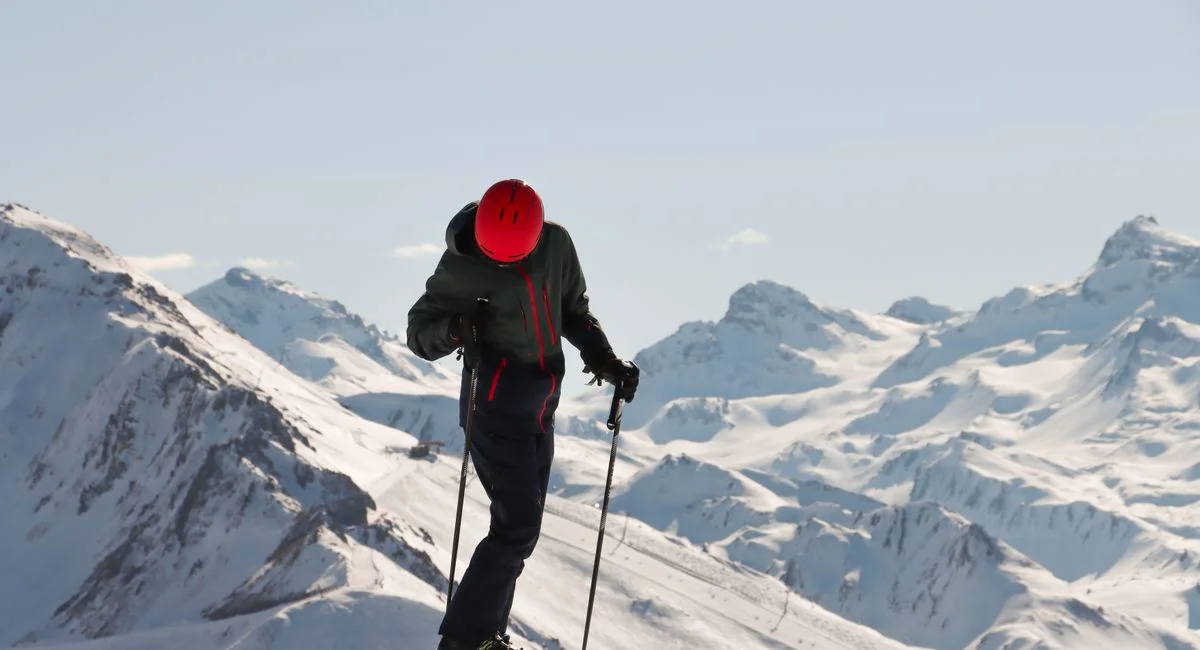 A skier with a red helmet enjoying a bright winter day on a snowy mountain.