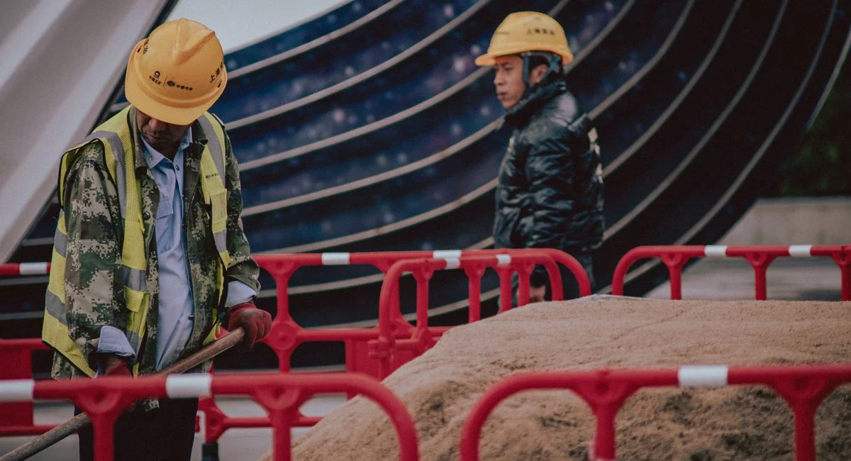 Construction workers with safety gear managing a sand pile outdoors on an urban site.