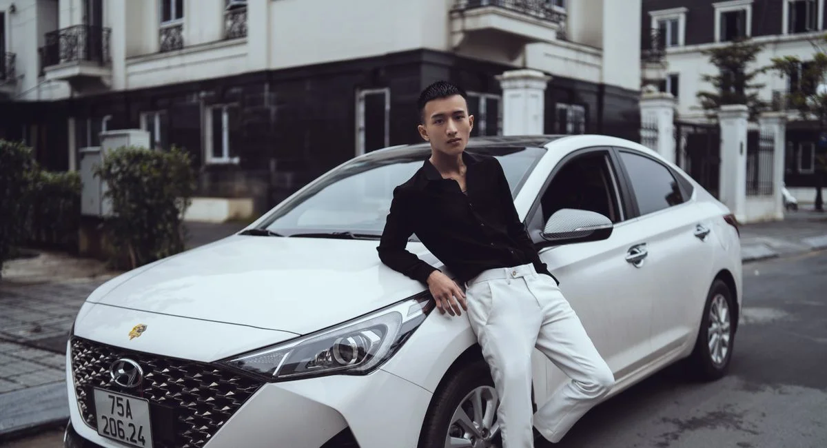 Trendy focused Asian male model in smart casual outfit leaning on sports car parked on road near building and looking at came