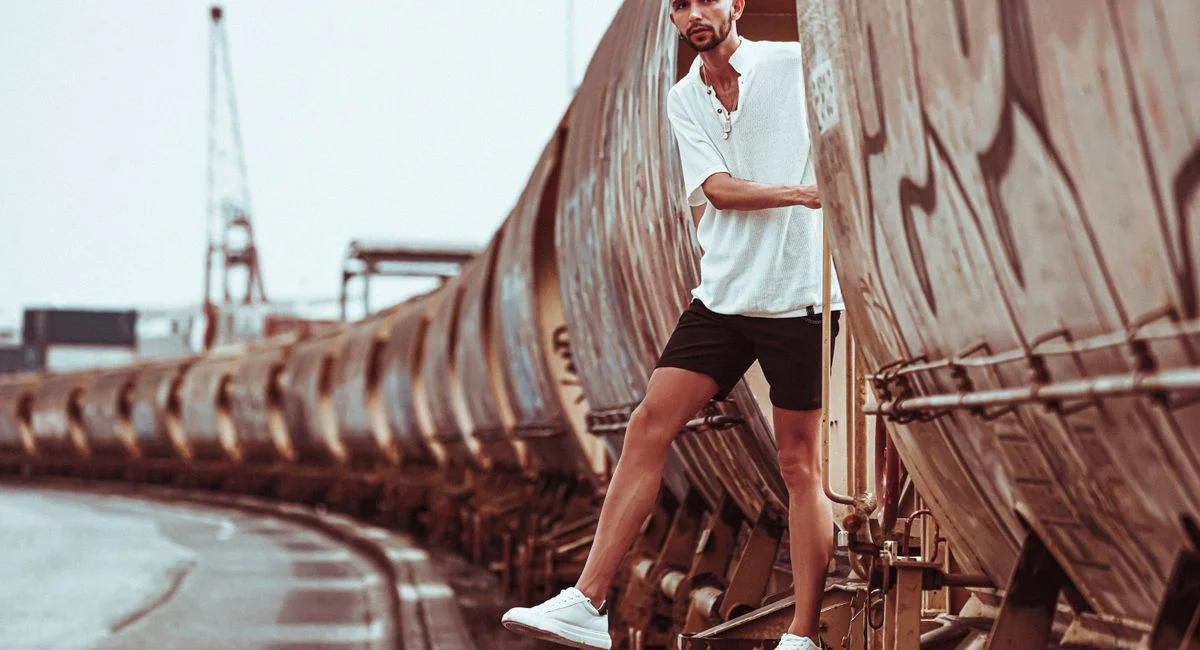 Confident man in white t-shirt and shorts standing on train, showcasing urban style and travel concept.