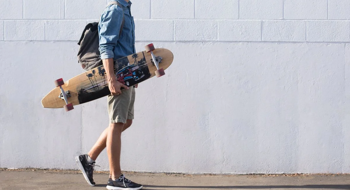 Casual young man walking with longboard against a white brick wall in Sanger, California.