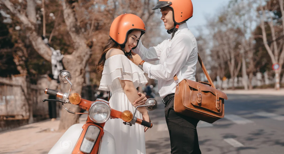A couple in helmets standing by a scooter on a sunny street in Dalat, Vietnam.