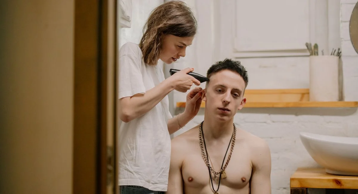Woman giving a young man a haircut at home, highlighting DIY haircare and grooming.