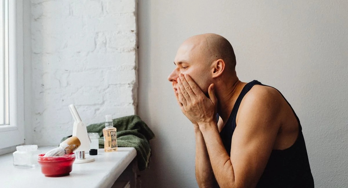 A man applies skincare in a natural-lit bathroom, reflecting self-care and grooming habits.