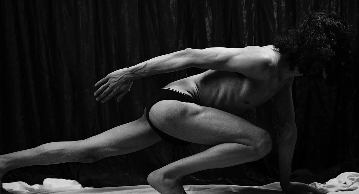 A monochrome image of a topless man in a dynamic stretch pose, showcasing musculature.