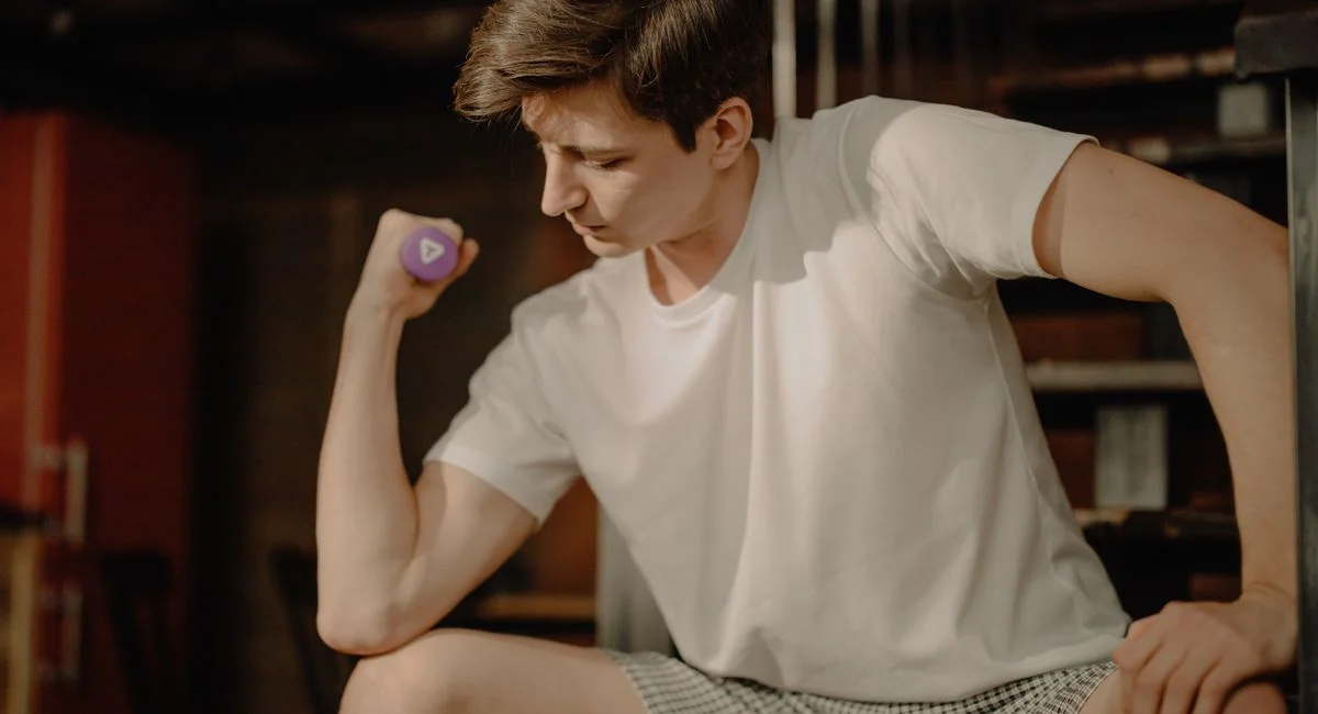 A young man performs a bicep curl with a dumbbell in a cozy home setting, focusing on fitness at home.