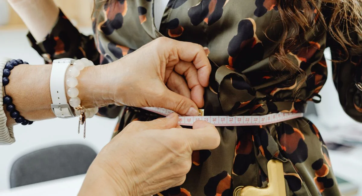 Tailor uses measuring tape on dress for perfect fit. Close-up fashion scene.