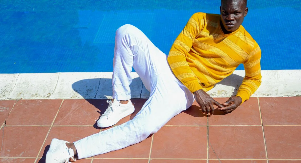 Fashionable man in a yellow sweater and white pants lounging by a poolside.