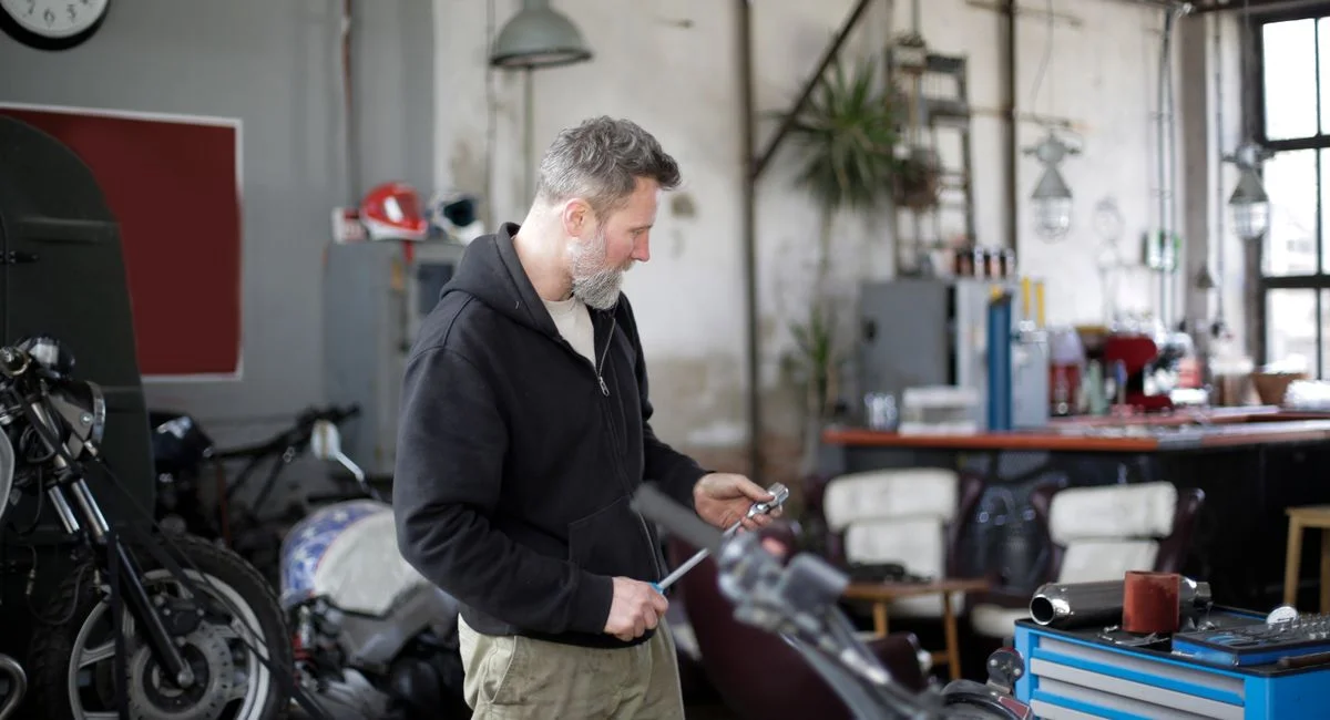 Side view of serious middle aged male mechanic in workwear standing with ratchet in modern garage while repairing motorbike